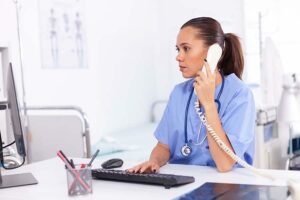 A picture of a Nurse attending to a patient on the phone while check her computer