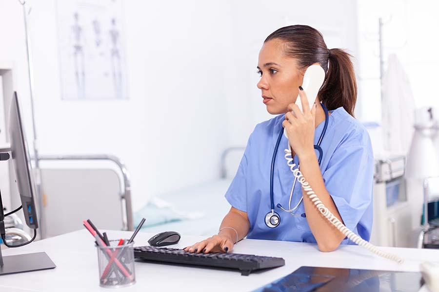 A picture of a Nurse attending to a patient on the phone while check her computer